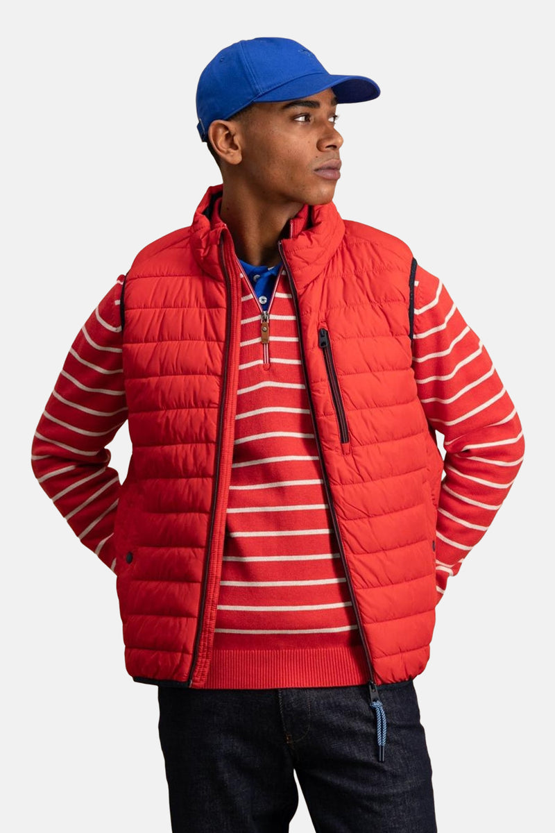 Veste sans manches rouge by FYNCH-HATTON, portée sur un pull rayé, avec une casquette bleue.