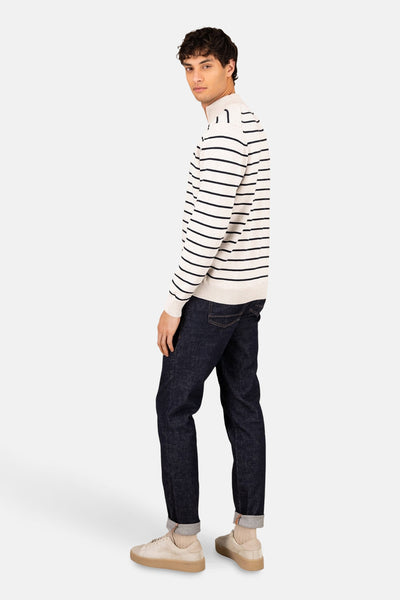 Pull col roulé écru de FYNCH-HATTON avec rayures bleu marine, porté avec un jean brut et des baskets beiges.