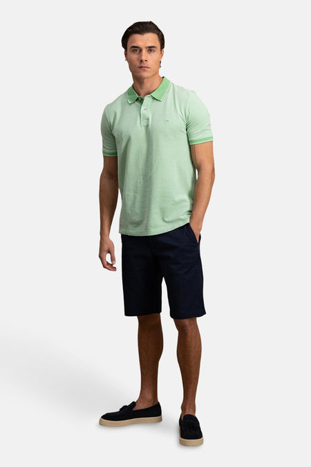 Polo à manches courtes vert de FYNCH-HATTON, porté avec un short bleu marine et des mocassins noirs.