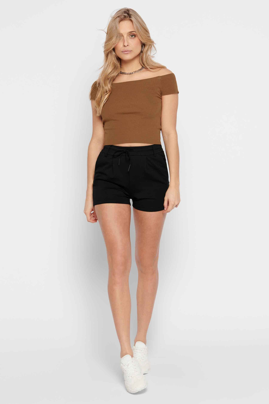 Zwarte korte broek van ONLY, gedragen met een bruine off-shoulder top en witte schoenen.