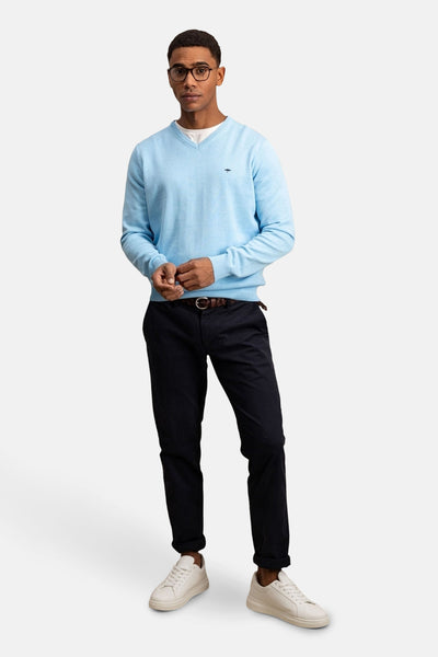 Pull à col en V bleu de FYNCH-HATTON porté avec un pantalon chino noir, une ceinture et des baskets blanches.
