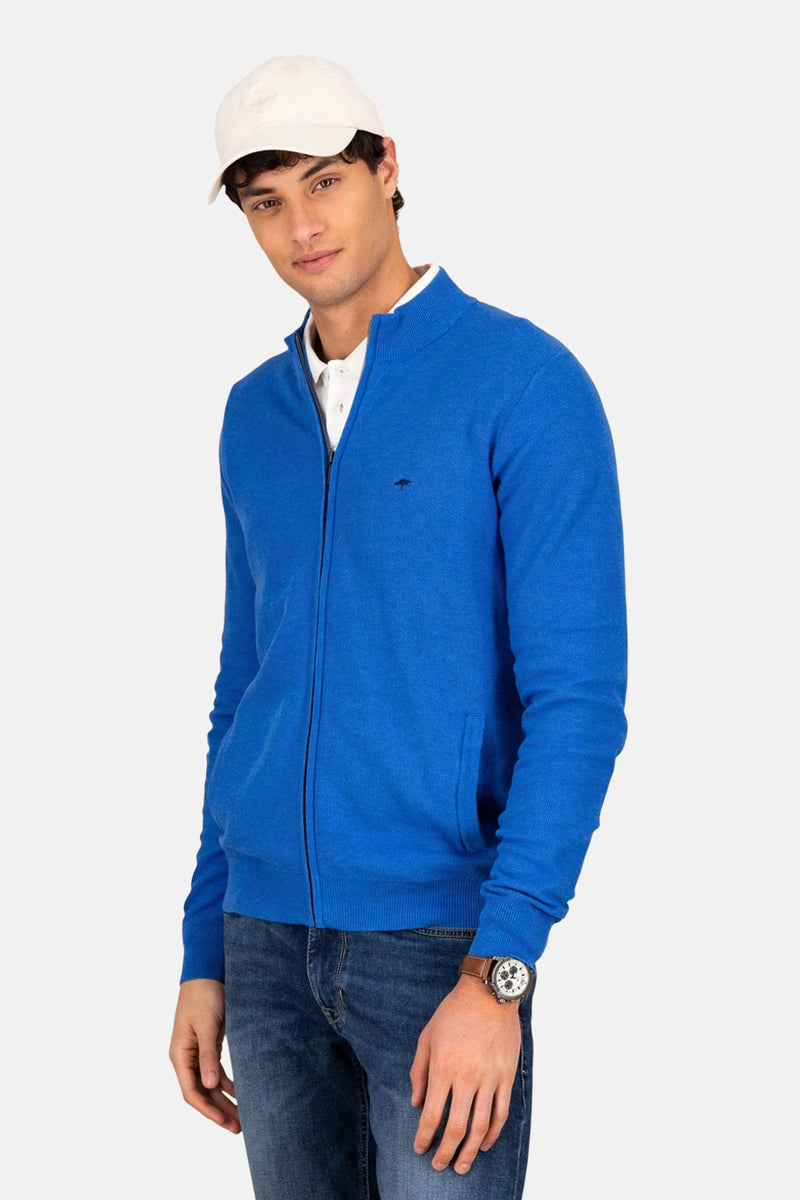 Gilet bleu de FYNCH-HATTON, porté avec un polo blanc et un jean, casquette blanche et montre.
