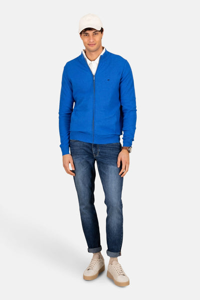 Gilet bleu par FYNCH-HATTON, porté avec un polo blanc, un jean et des baskets beiges.