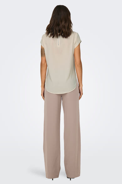 Chemisier beige à manches courtes de ONLY, avec fermeture éclair au dos et porté avec un pantalon beige large.