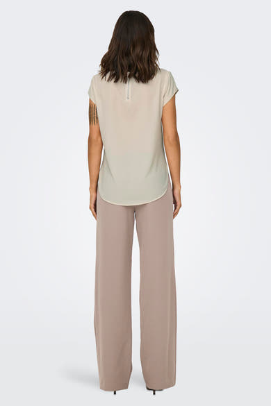 Blouse beige à manches courtes de ONLY, avec fermeture éclair apparente dans le dos, portée avec un pantalon fluide beige.