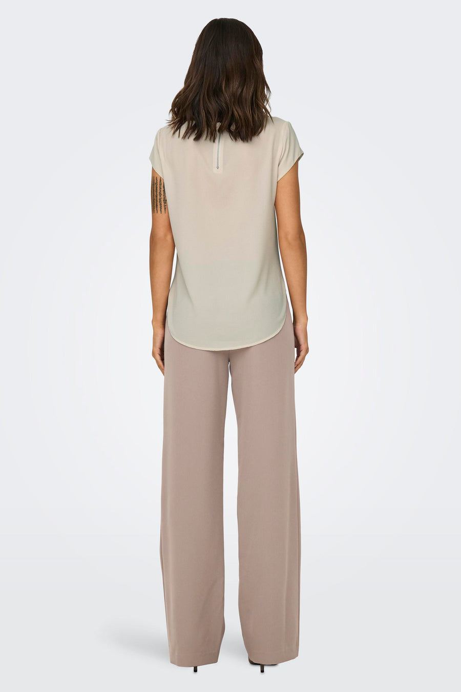 Blouse beige à manches courtes de ONLY, avec fermeture éclair apparente dans le dos, portée avec un pantalon fluide beige.