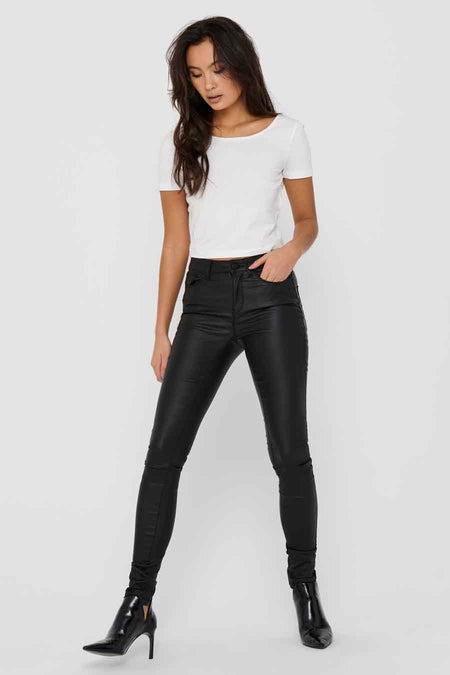 Pantalon noir brillant de ONLY, porté avec un t-shirt blanc uni et des bottines noires à talons.
