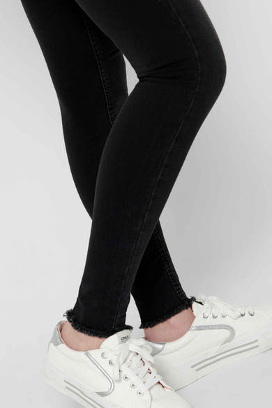 Skinny jeans in zwart denim van ONLY, met rafelige zoom, gedragen met witte sneakers met zilveren strepen.