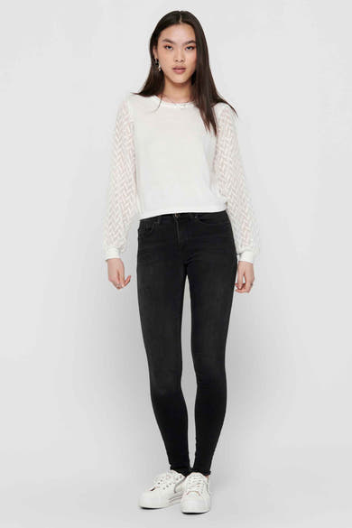 Zwarte skinny jeans van ONLY, gedragen met een witte top met doorschijnende mouwen en witte sneakers.