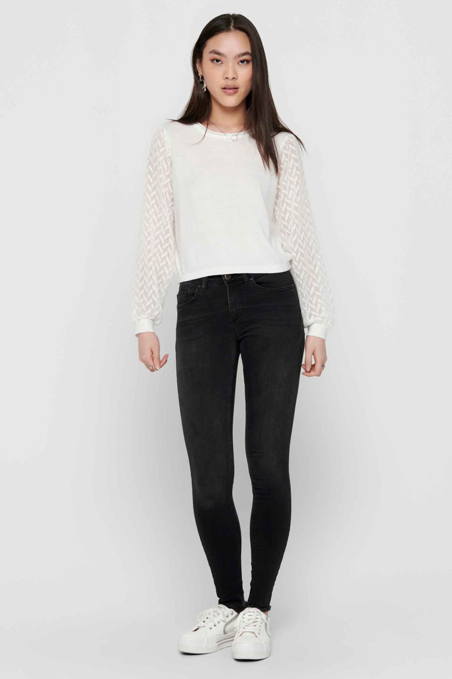 Zwarte skinny jeans van ONLY, gedragen met een witte top met doorschijnende mouwen en witte sneakers.