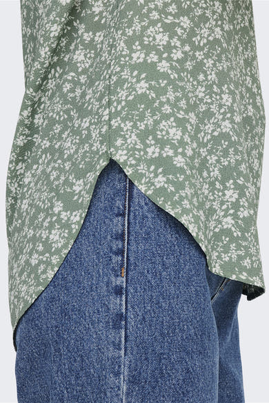 Blouse multicolore à manches courtes de ONLY, à motif floral sur fond vert, portée avec un jean bleu.
