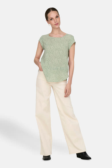Chemisier vert à manches courtes de ONLY, avec motif imprimé, porté avec un pantalon clair et des bottines noires.

