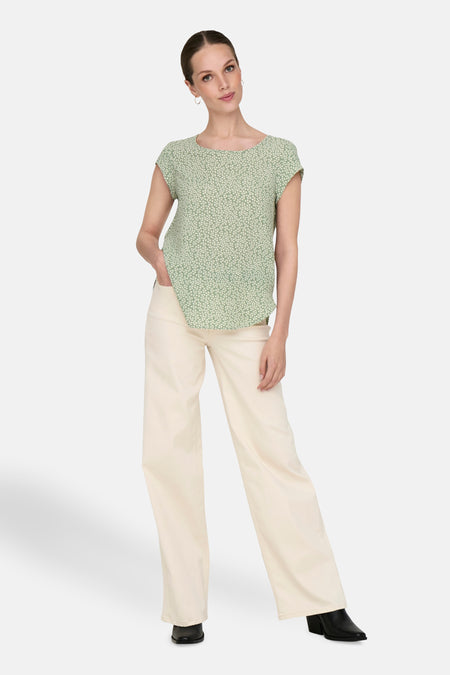Chemisier vert à manches courtes de ONLY, avec motif imprimé, porté avec un pantalon clair et des bottines noires.
