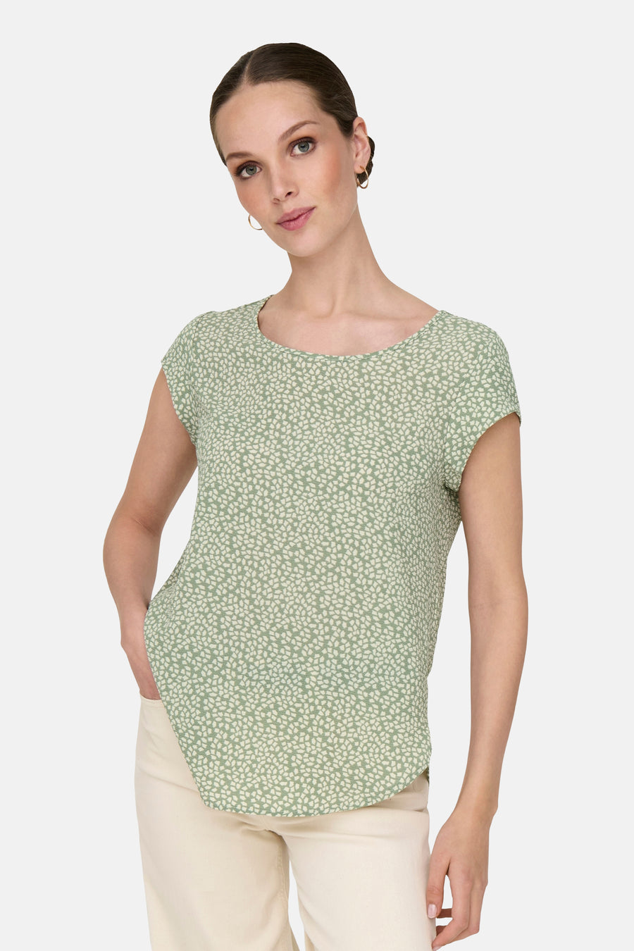 Chemisier vert à manches courtes par ONLY, imprimé de motifs végétaux, porté avec un pantalon clair et des boucles d'oreilles dorées.