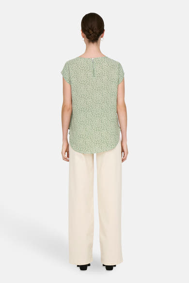 Chemisier vert à manches courtes de ONLY® avec un motif floral, porté avec un pantalon beige et des chaussures noires, vue de dos.
