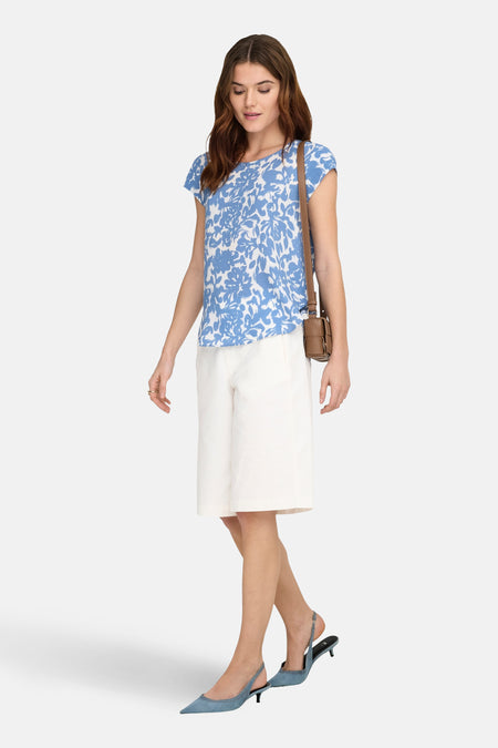 Chemisier à manches courtes par ONLY®, à imprimé fleuri bleu, porté avec un short blanc et un sac bandoulière marron.