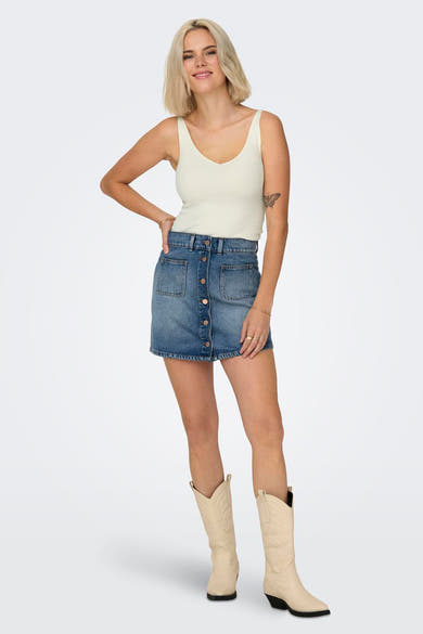 Débardeur blanc de JDY en maille côtelée, porté avec une jupe en jean boutonnée et des bottes de cow-boy beiges.