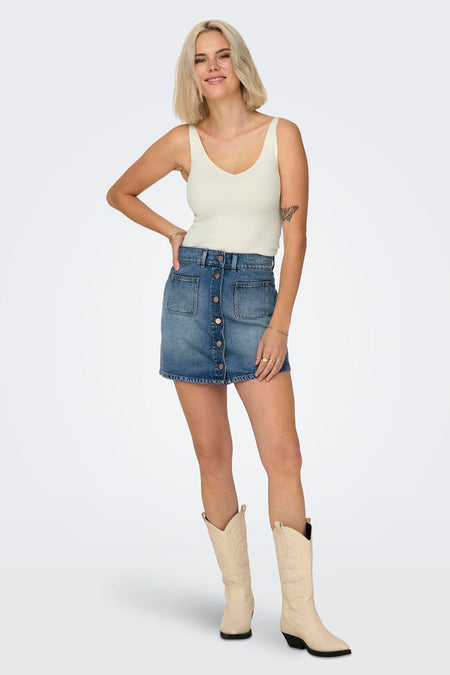 Débardeur blanc de JDY en maille côtelée, porté avec une jupe en jean boutonnée et des bottes de cow-boy beiges.