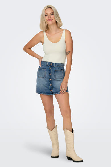 Débardeur blanc de JDY, porté avec une jupe en jean boutonnée et des bottes de cow-boy.