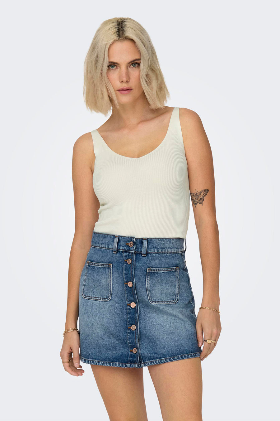 Débardeur blanc de JDY, côtelé, porté avec une jupe en jean boutonnée et des bijoux dorés.
