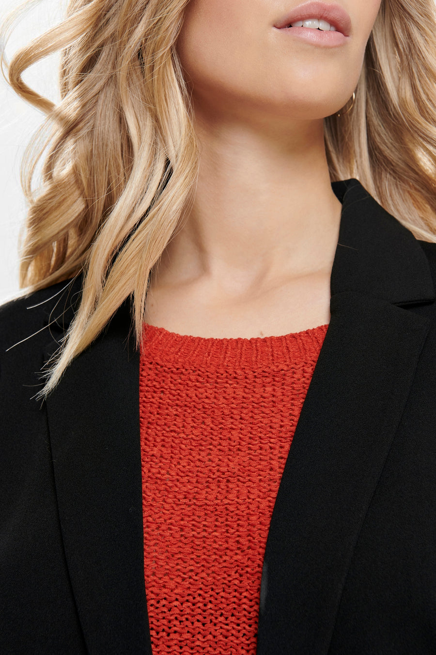 Zwarte blazer van JDY gedragen over een oranje, getextureerde trui, detail op het bovenlichaam.