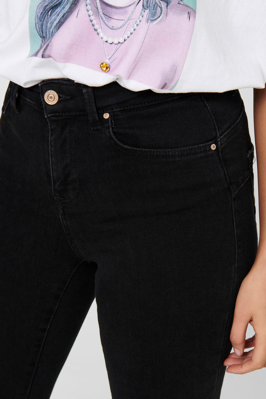 Jean skinny noir de ONLY, détail de la taille haute, porté avec un t-shirt imprimé.
