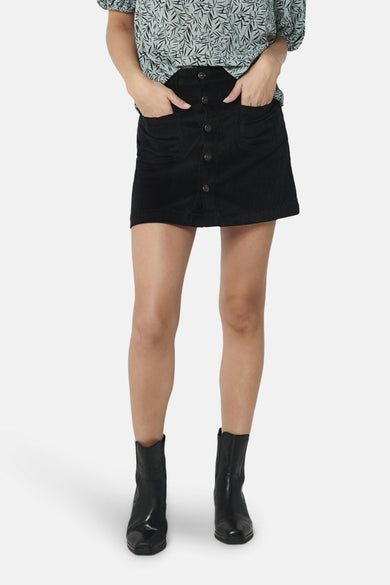 Jupe courte noire en velours côtelé de ONLY, avec poches plaquées et boutonnée sur le devant, portée avec un chemisier imprimé et des bottines noires.