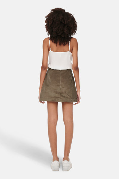 Bruine korte bruine corduroy rok van ONLY, met een witte top met spaghettibandjes en witte sneakers.