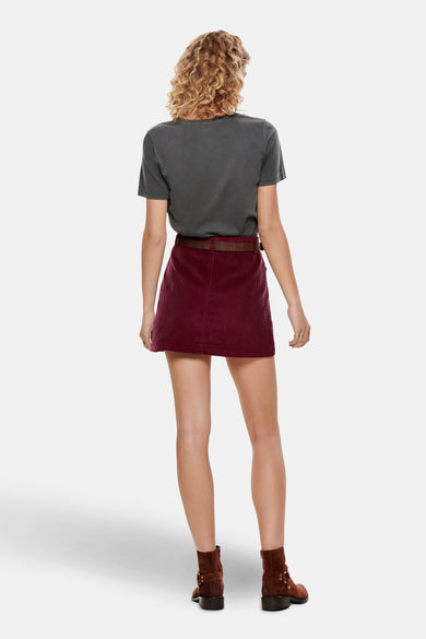 Korte bordeauxrode corduroy rok van ONLY, gedragen met een grijs T-shirt, een bruine riem en bruine suède enkellaarsjes.