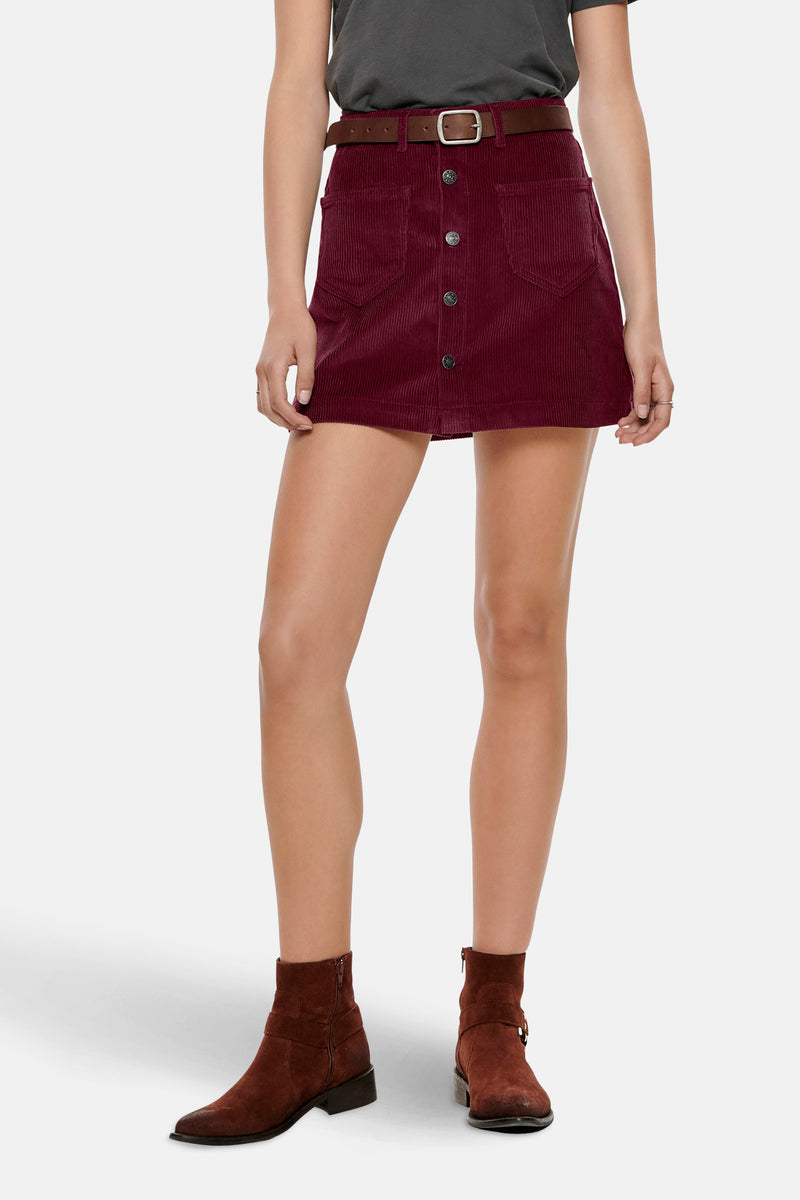 Korte bordeauxrode corduroy rok van ONLY, met bruine riem en bruine enkellaarsjes.