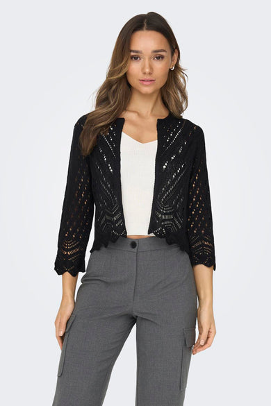 Cardigan noir en maille ajourée de JDY, porté sur un débardeur blanc et un pantalon gris.
