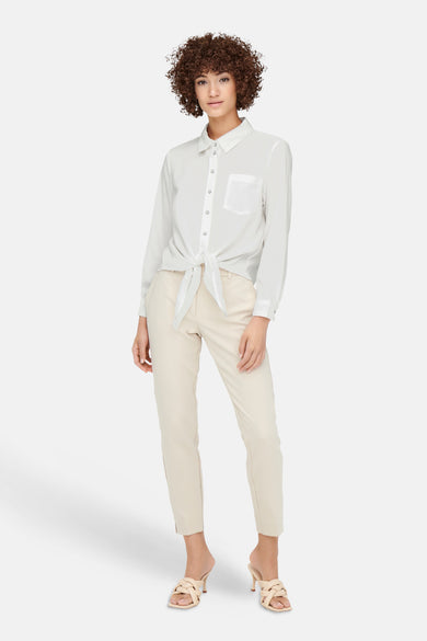 Chemisier blanc (manches longues) de ONLY, noué à la taille, avec un pantalon beige et des mules à talons tressées.
