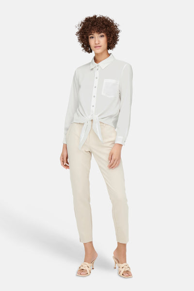 Chemisier blanc (manches longues) de ONLY, noué à la taille, avec un pantalon beige et des mules à talons tressées.
