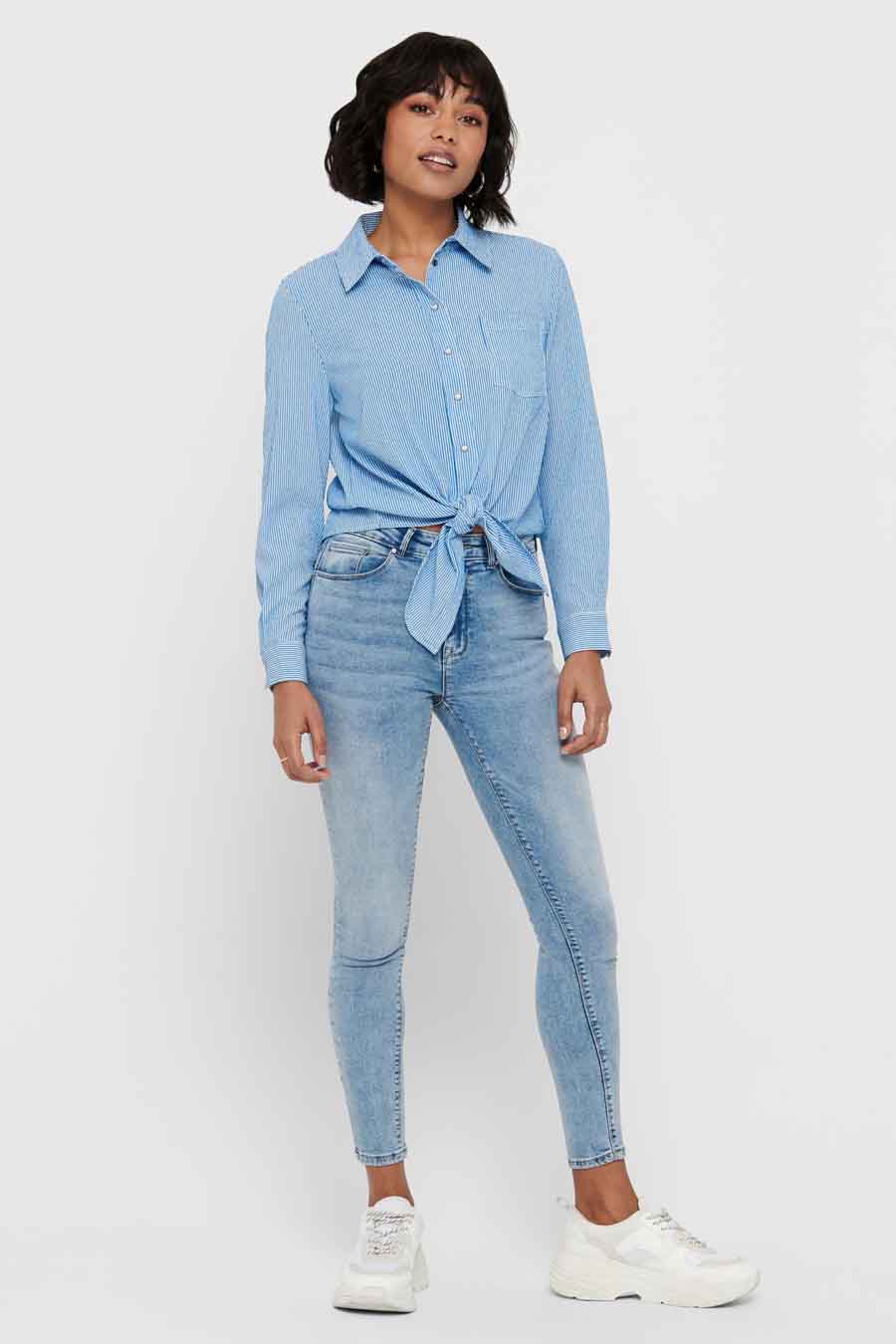 Chemise bleue rayée à manches longues par ONLY, nouée à la taille, portée avec un jean et des baskets blanches.