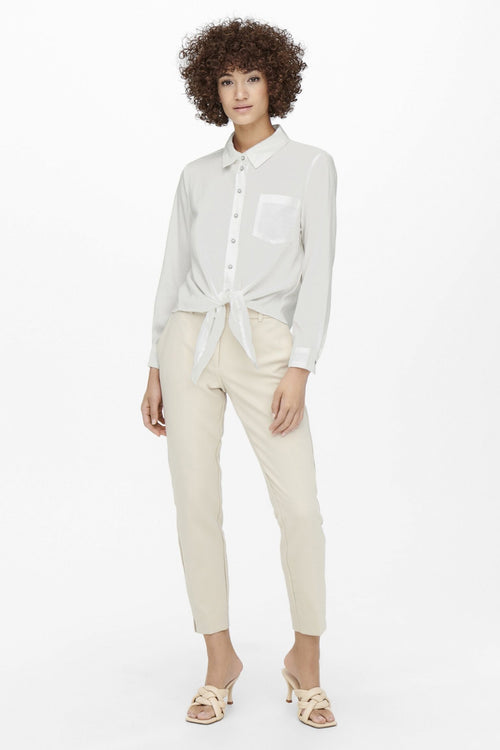 Chemisier bleu à manches longues de ONLY®, noué à la taille, porté avec un pantalon beige et des mules.
