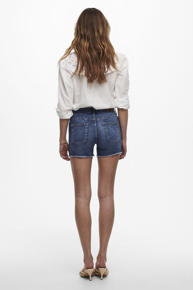 Short bleu de ONLY, porté avec une chemise blanche et des mules à talons.