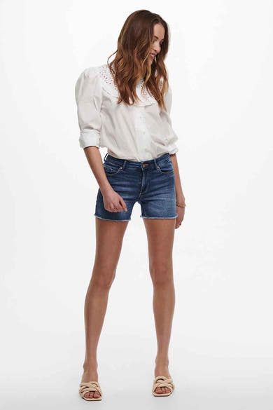 Short bleu de ONLY®, porté avec un chemisier blanc et des sandales beiges.
