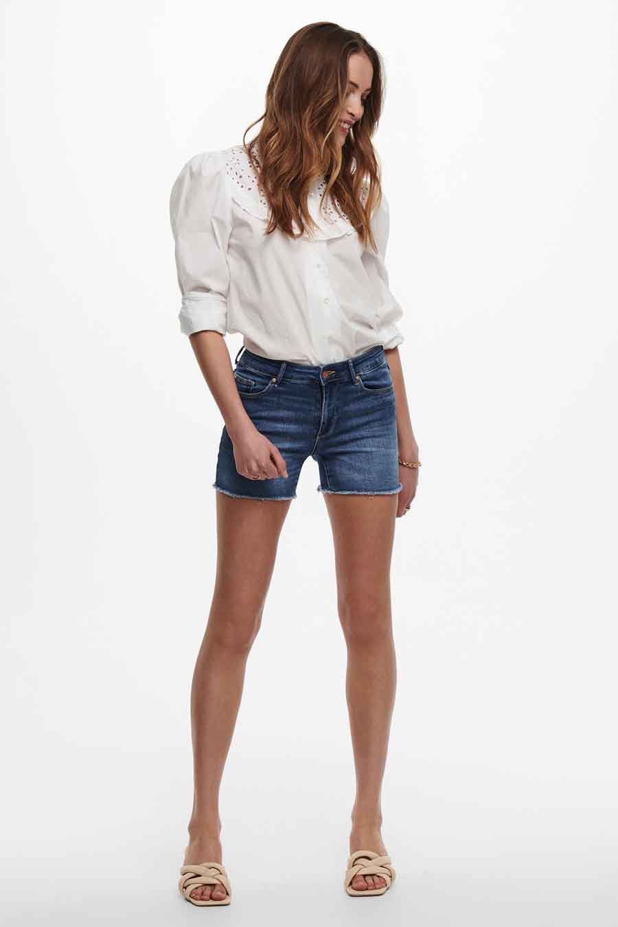 Short bleu de ONLY®, porté avec un chemisier blanc et des sandales beiges.

