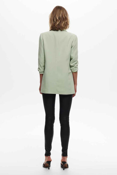 Blazer vert clair de ONLY, porté avec un pantalon noir moulant et des escarpins noirs, vue de dos.

