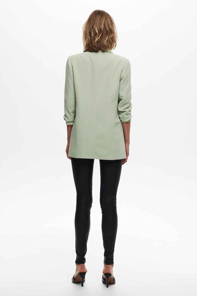 Blazer vert clair de ONLY, porté avec un pantalon noir moulant et des escarpins noirs, vue de dos.
