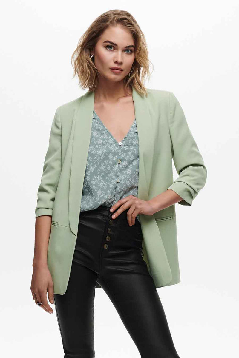 Blazer vert d'ONLY, porté sur un chemisier à fleurs bleu clair et un pantalon noir à boutons.
