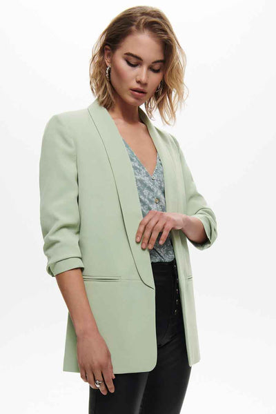 Blazer vert clair de ONLY avec manches trois-quarts roulées, porté sur un chemisier à motif floral.