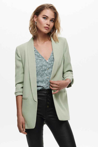 Blazer vert de ONLY, avec une coupe décontractée, porté sur un chemisier à motif floral et un pantalon noir.
