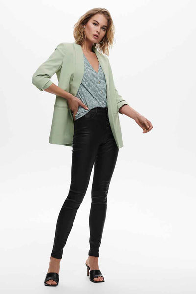 Blazer vert de ONLY®, porté avec un chemisier à motif et un pantalon noir moulant.
