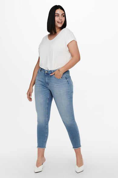 Jean skinny bleu moyen denim de CARMAKOMA, porté avec un t-shirt blanc et des mules blanches pointues.