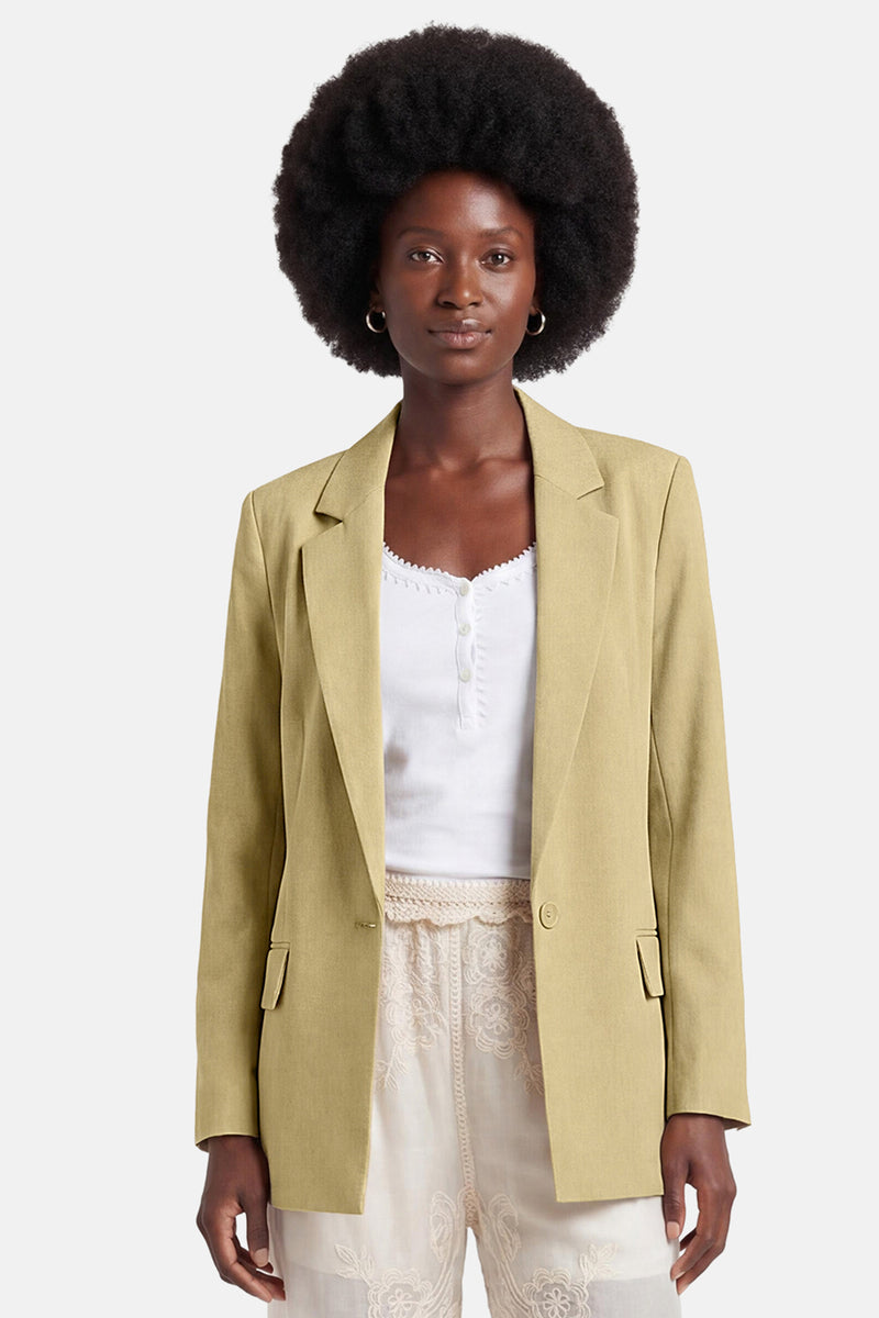 Blazer vert clair de GOA GOA, coupe droite à un bouton, avec poches à rabat, porté sur un haut blanc et un pantalon brodé.
