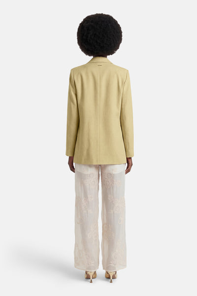 Blazer vert clair de GOA GOA vu de dos, avec le nom GIANA brodé sur le col, porté sur un pantalon brodé et des talons dorés.