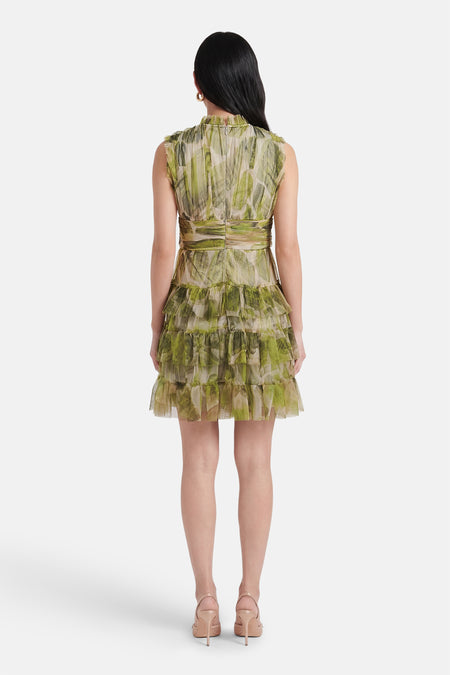 Robe courte verte de GOA GOA, à motifs abstraits, avec des volants étagés et des escarpins couleur chair.
