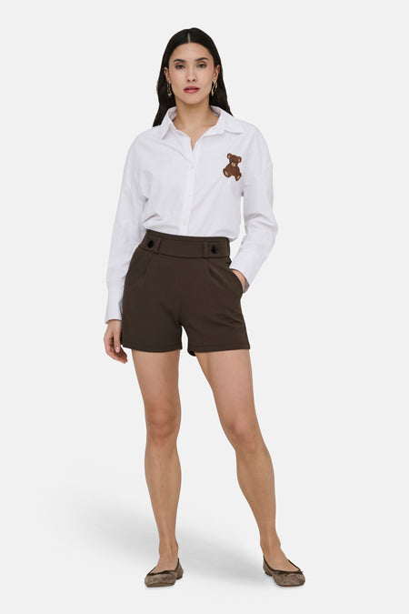 Short brun de JDY, porté avec une chemise blanche agrémentée d'un ours en peluche et des ballerines marron.
