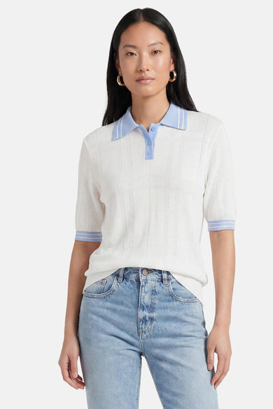 Pull polo blanc ajouré et bleu clair de GOA GOA, avec col et bords de manches rayés, porté avec un jean.